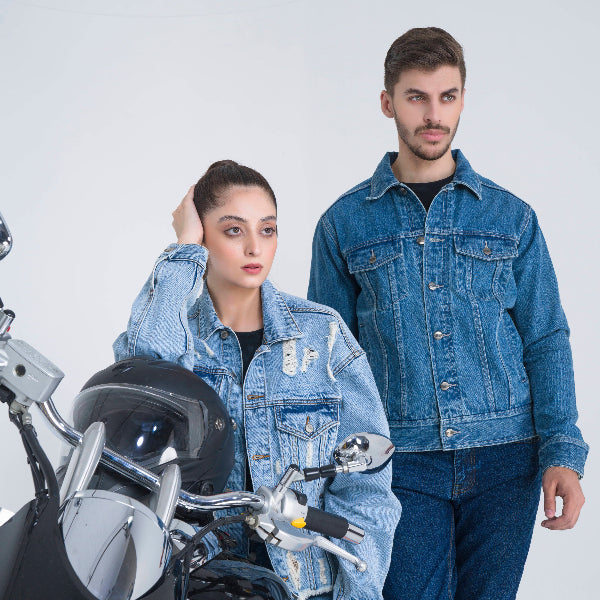 Two people wearing denim jackets standing next to a motorcycle on a white background