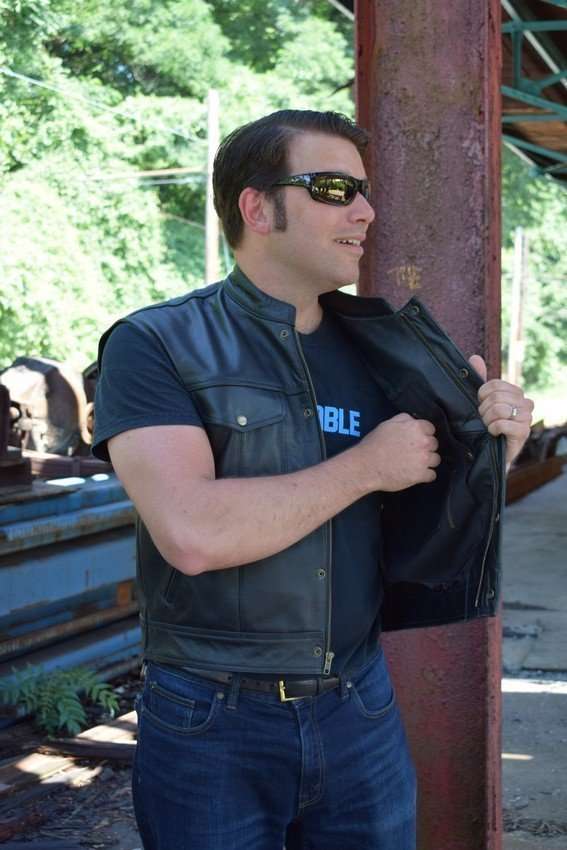 A model wears a black leather motorcycle vest featuring front pockets, a zip, and a polyester lining
